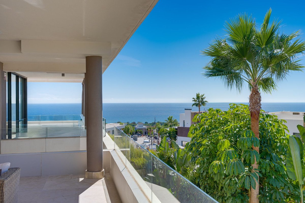 Spacious balcony with sea view, palm trees, and modern glass railings, overlooking a coastal town.