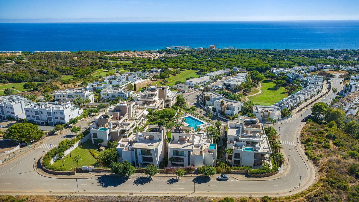 Aerial view of modern white apartment buildings with private pools, surrounded by green golf courses and the blue sea in the distance.