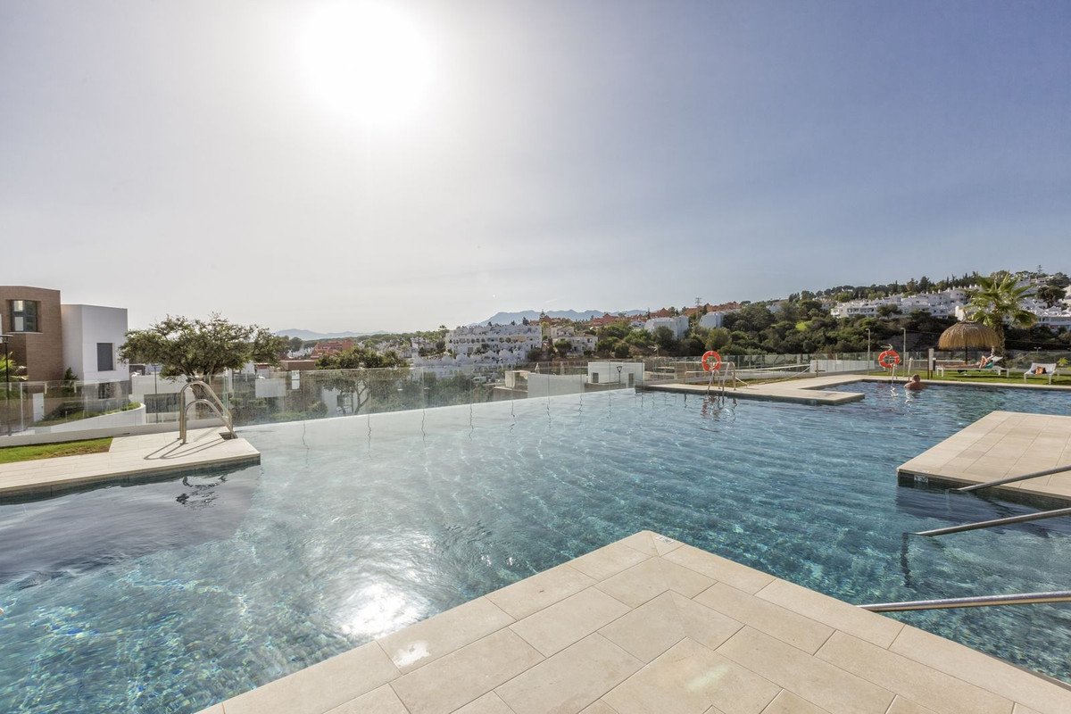 Infinity pool overlooking a hillside town with white buildings under a sunny sky. Features lounge chairs and a thatched umbrella.