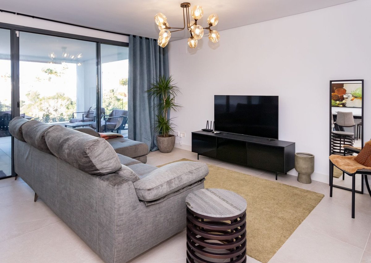 Modern living room with a large grey sectional sofa, entertainment unit with a TV, and sliding glass doors opening to an outdoor seating area.