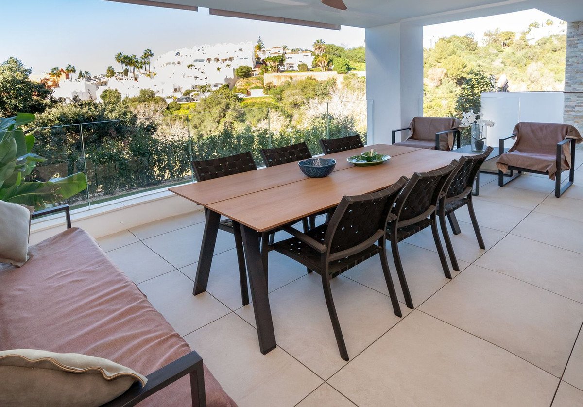A spacious terrace with a dining table, chairs, and a lounge bed, offering a beautiful view of a hillside town.