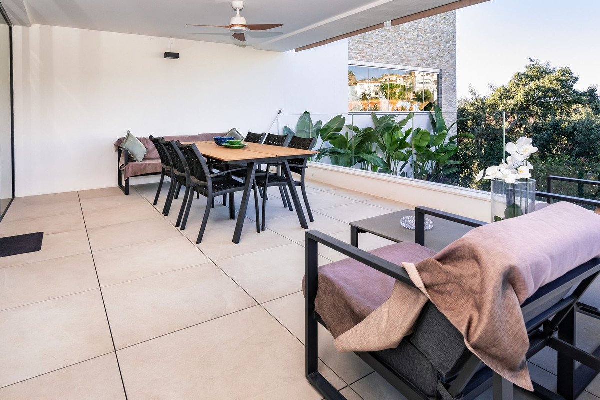 Modern terrace with dining table, seating area, lush plants, and a view of buildings and trees.
