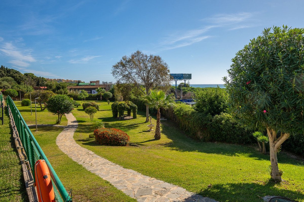 Garden with stone path, green lawn, trees, and distant sea view under blue sky