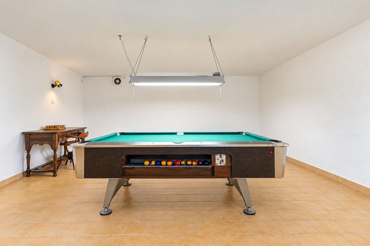 A game room with a pool table, wooden floor, and a small table with chairs.