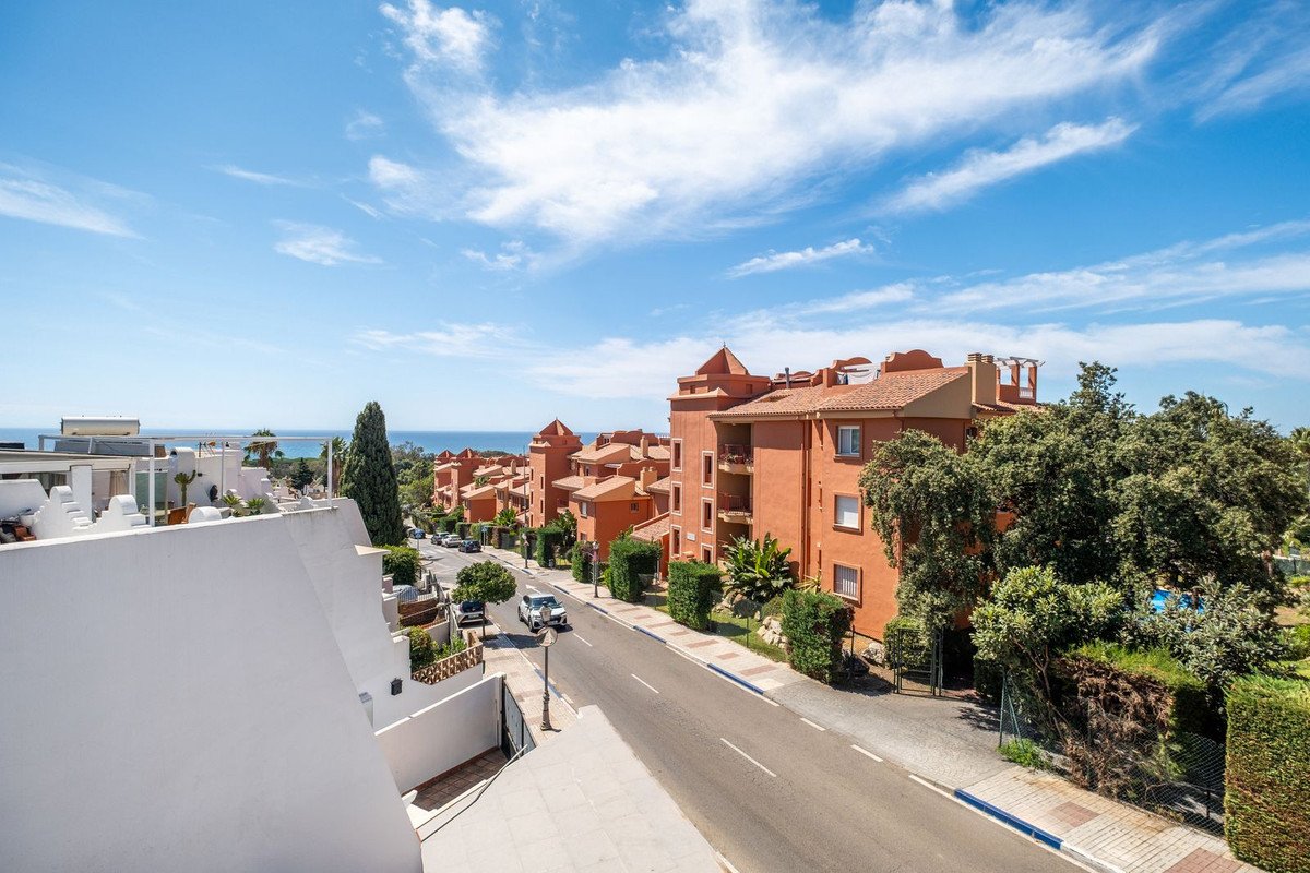 View of orange buildings with balconies and a distant sea view under a blue sky with clouds.