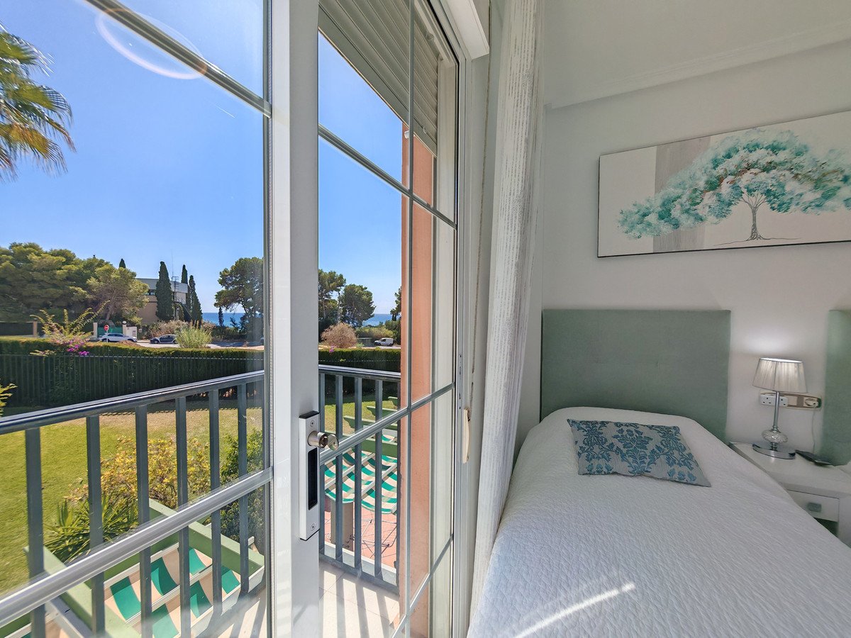 Bedroom with a single bed, a picture of a tree on the wall, and a balcony with a view of the sea and garden.