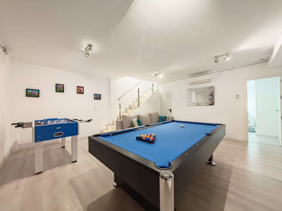 Spacious recreation room with a blue pool table, foosball table, and comfortable sofa. Modern interior with stairs in the background.