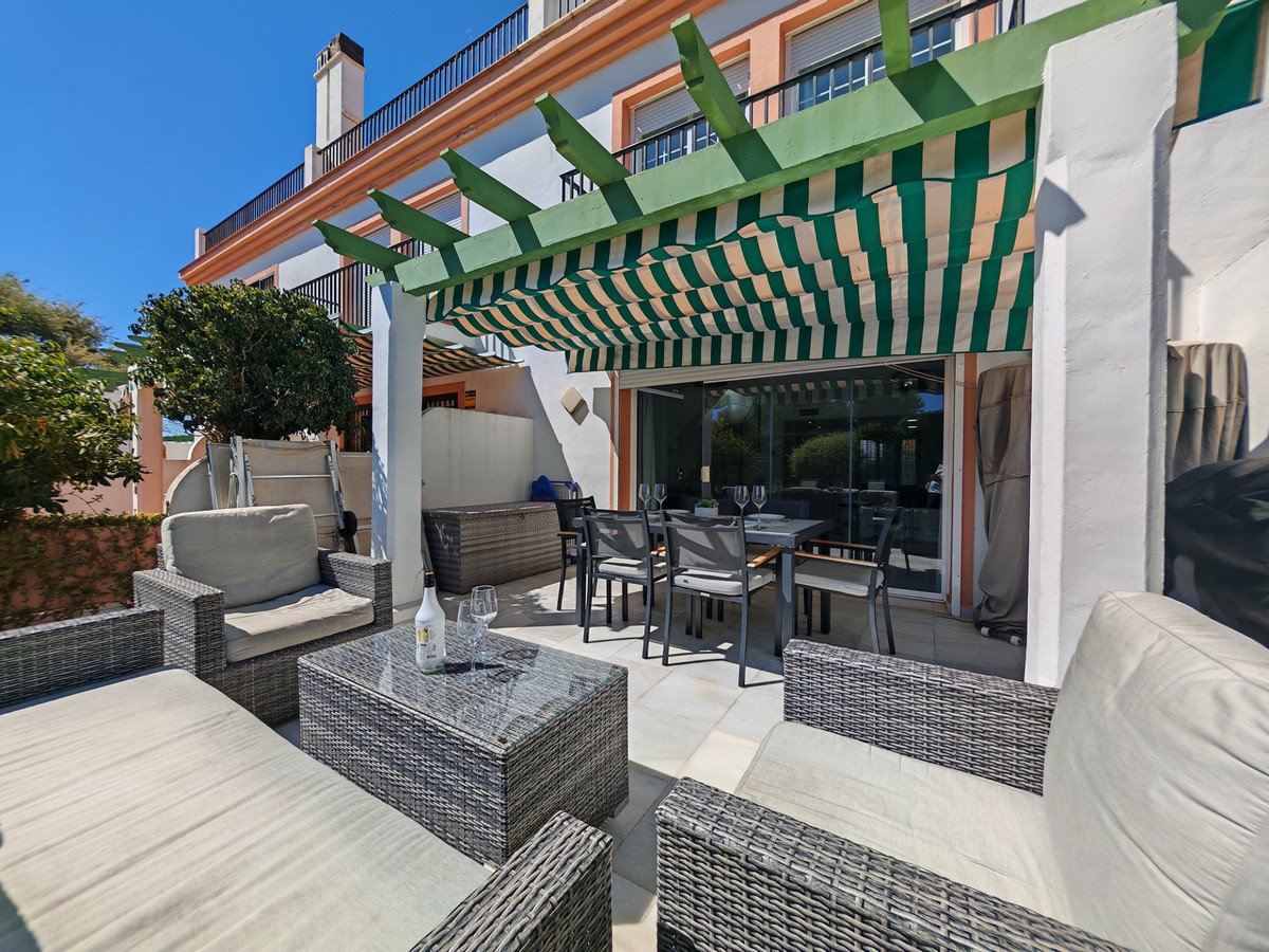 Spacious terrace with outdoor dining set, lounge seating, and a striped awning providing shade on a sunny day.