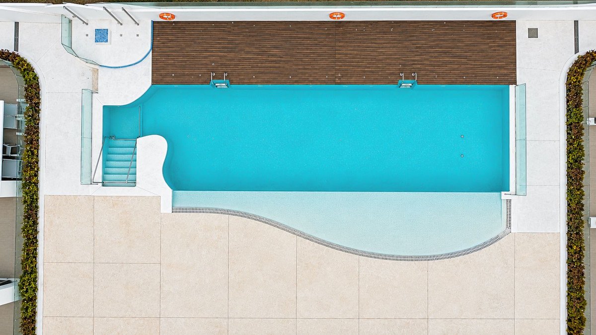 Aerial view of a modern swimming pool with wooden deck and tiled patio.
