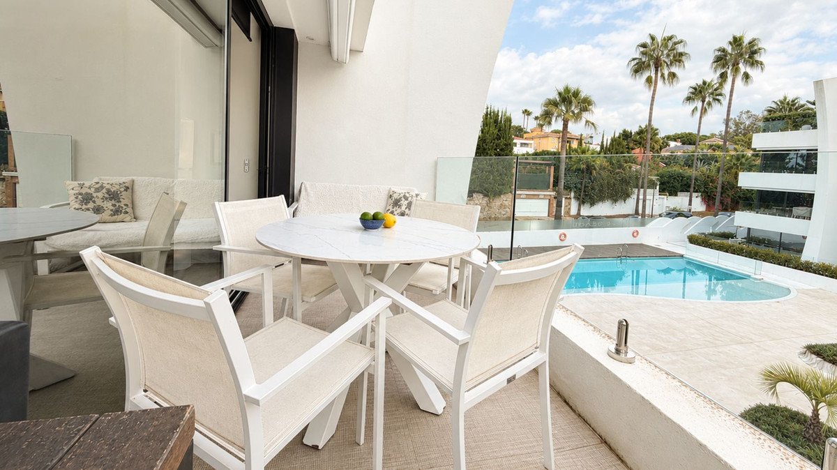 Balcony with dining table and chairs overlooking a swimming pool and palm trees
