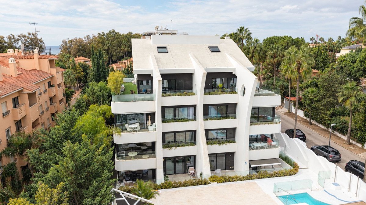 Modern multi-story apartment building with balconies, pool, and green surroundings