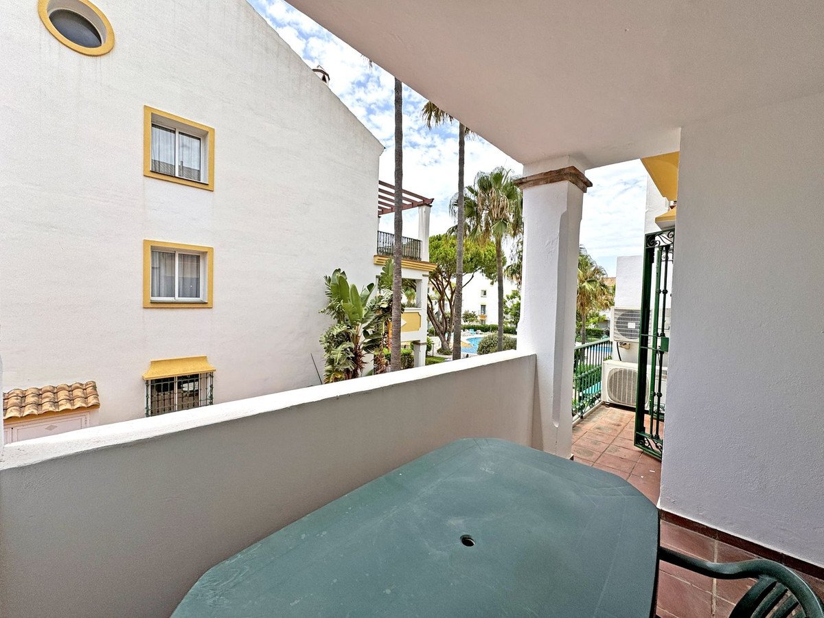 Balcony view with a table and chair overlooking palm trees, pool, and neighboring buildings.