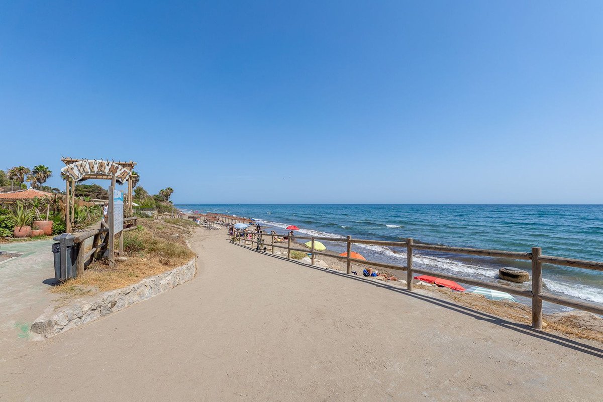 Sandy beach path with wooden fence and the blue ocean under a clear sky. People relaxing on the beach.