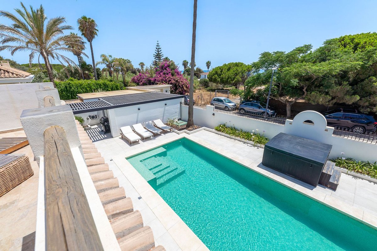 A private swimming pool with steps, surrounded by a paved patio and sun loungers, with lush greenery and palm trees in the background.