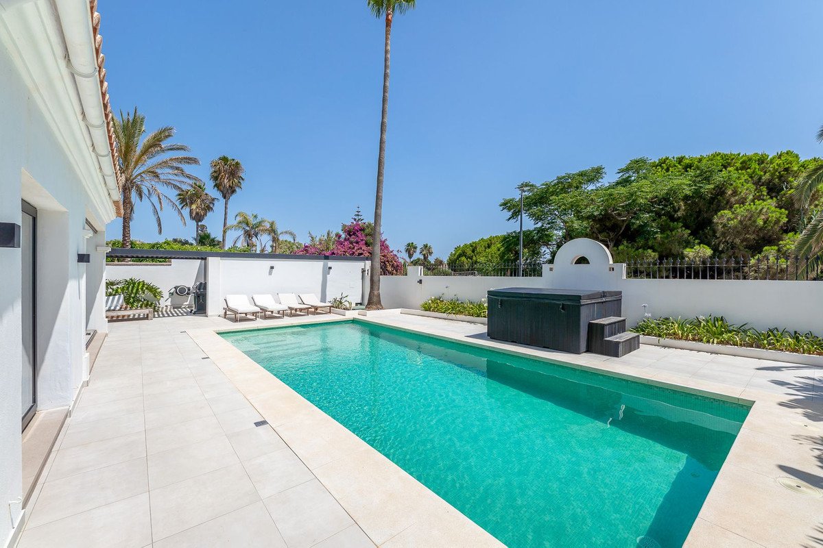A large swimming pool with a hot tub, loungers, and palm trees in a sunny outdoor area.