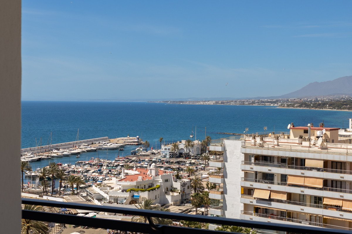 Sea view from balcony, marina, boats, palm trees, and coastal buildings under clear blue sky.