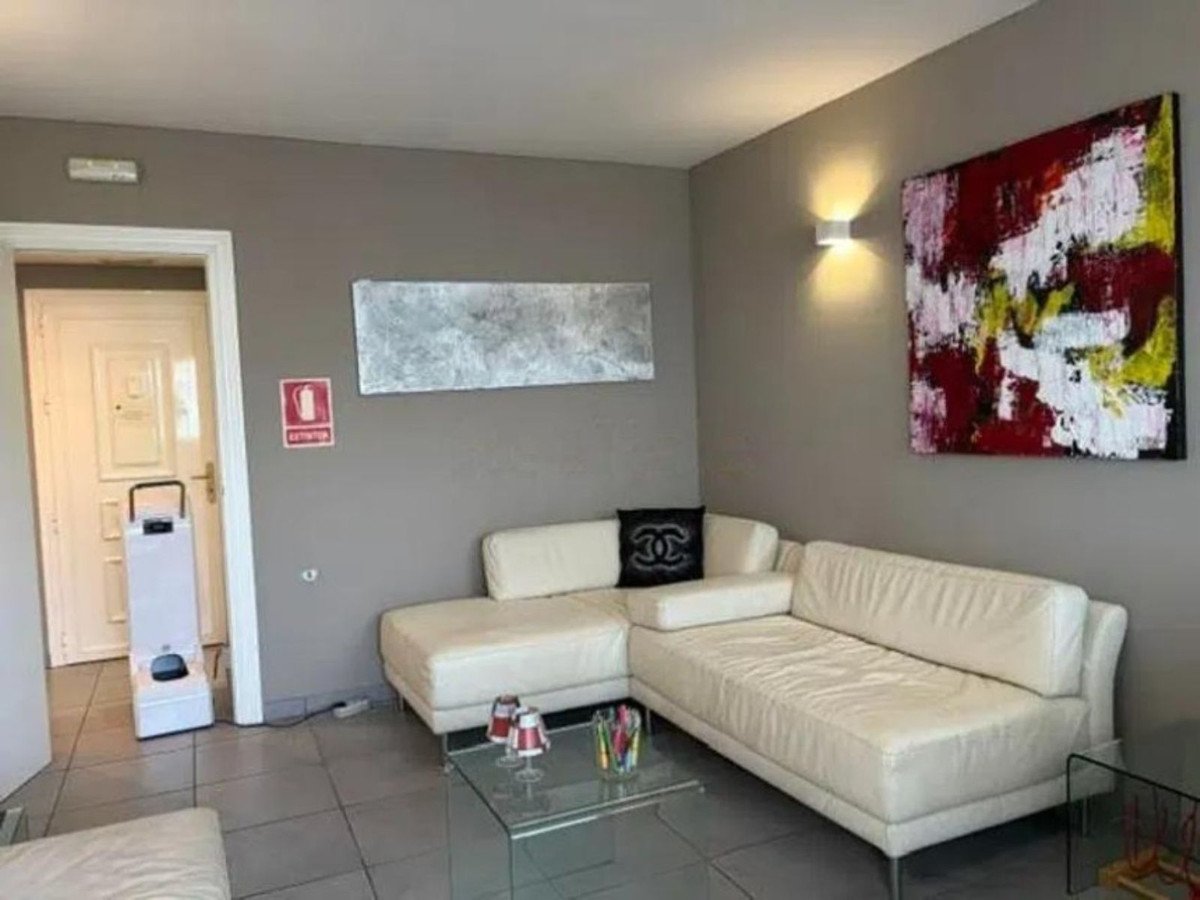 Modern living room with a large white sectional sofa, abstract art on the wall, and a glass coffee table.