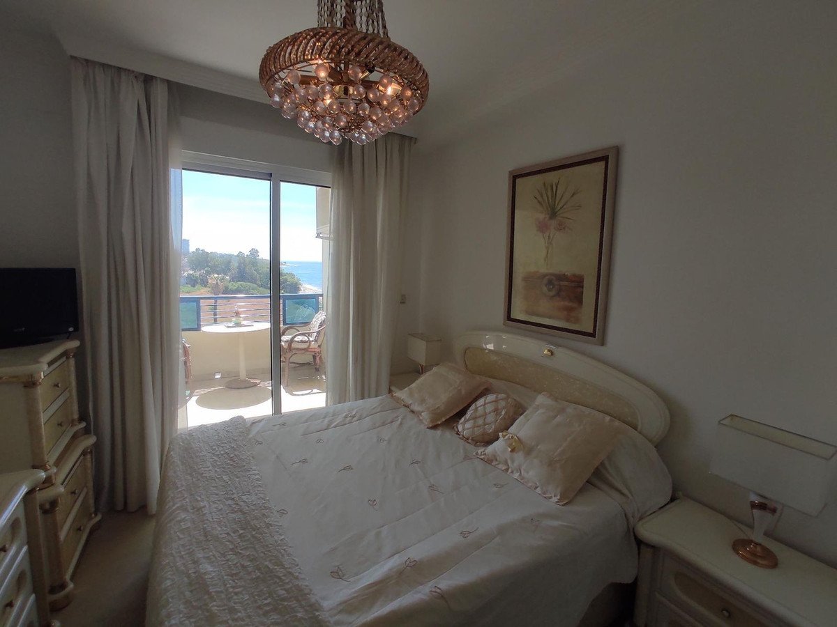 Bedroom with king-size bed, chandelier, and sliding doors opening to a balcony with a sea view.