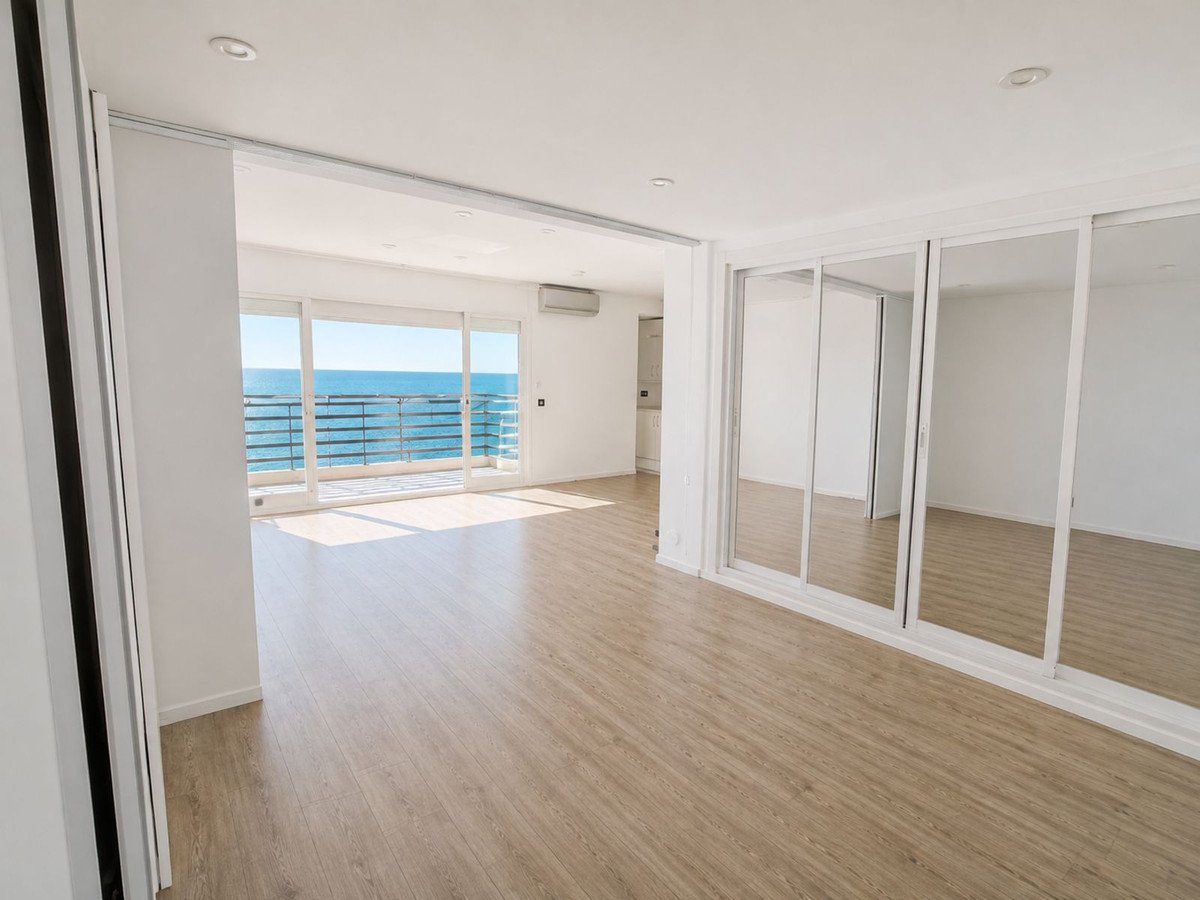 Spacious living room with large sliding glass doors offering a balcony and ocean view, featuring mirrored closets and light wood flooring.