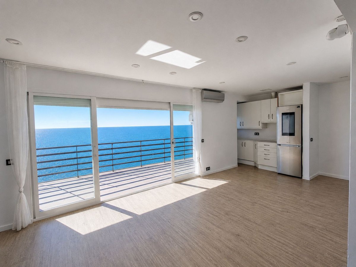 Living room and kitchen area with large sliding doors opening to a balcony with a stunning sea view.