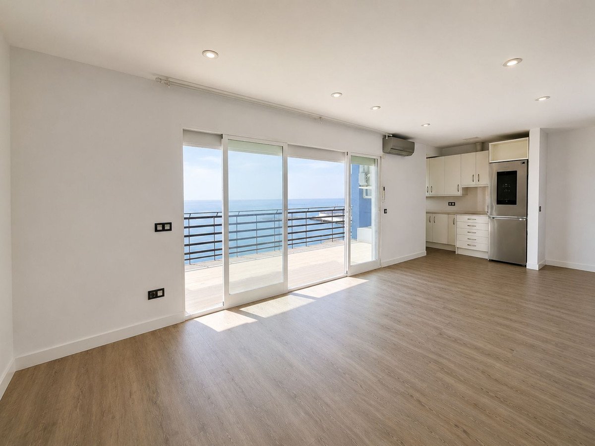 Spacious living area with large sliding glass doors opening to a balcony with a sea view. Modern kitchen area visible.
