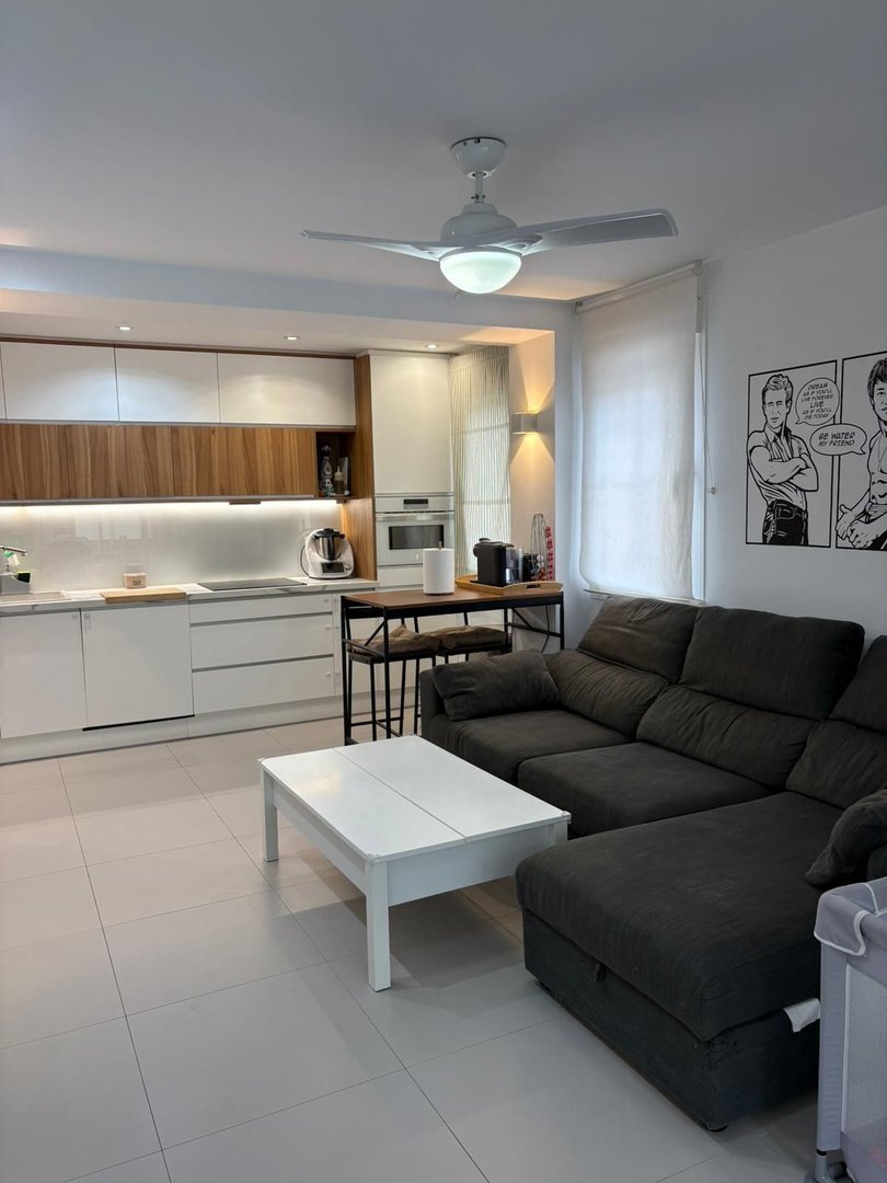 Modern kitchen and living room with a dark sectional sofa, white coffee table, and built-in cabinets.