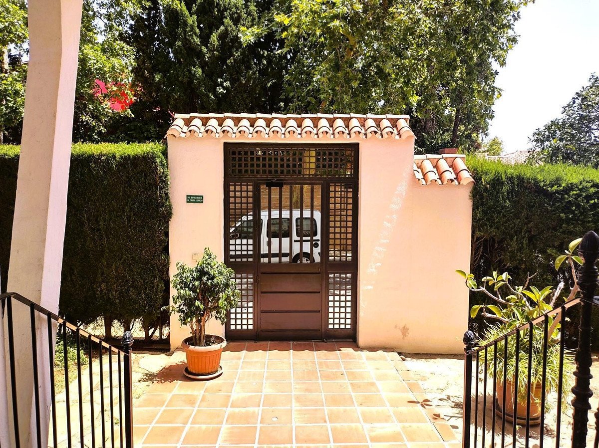 Entrance gate with a van visible behind, surrounded by hedges and potted plants.