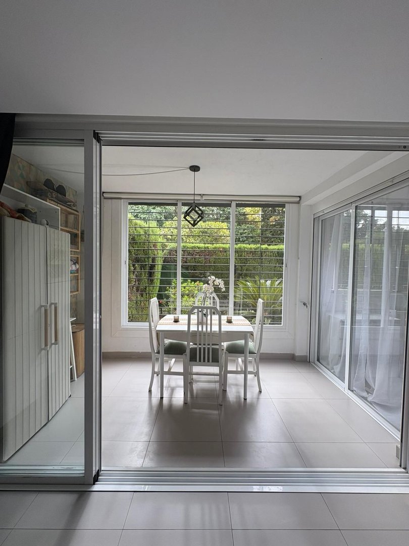 A dining room with a table and chairs set for four, featuring a beautiful garden view through large windows.