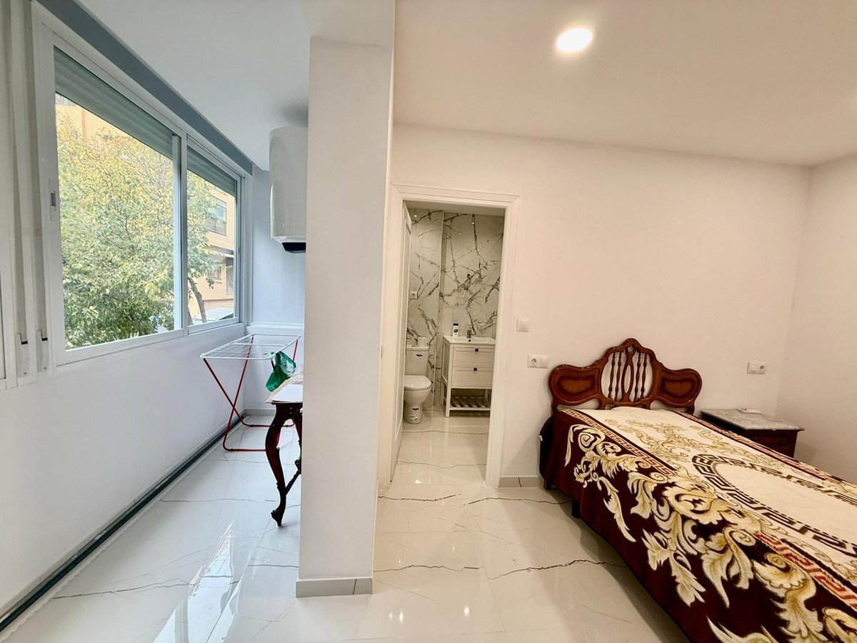 A bedroom with a wooden bed, marble flooring, and a view of greenery through a large window.