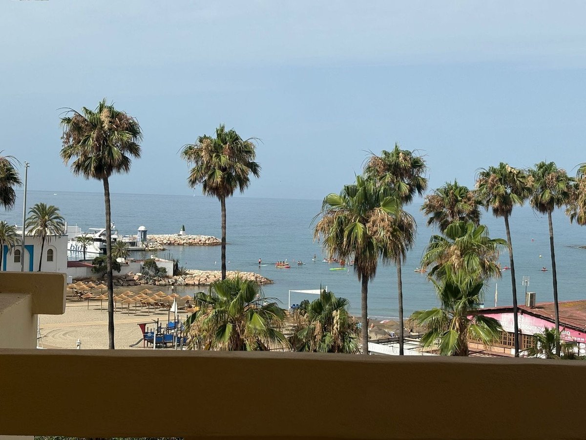Balcony view of a beach with palm trees, ocean, and people swimming.