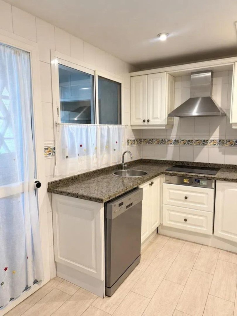 A compact kitchen featuring white cabinets, granite countertops, a stainless steel range hood, and a built-in dishwasher.
