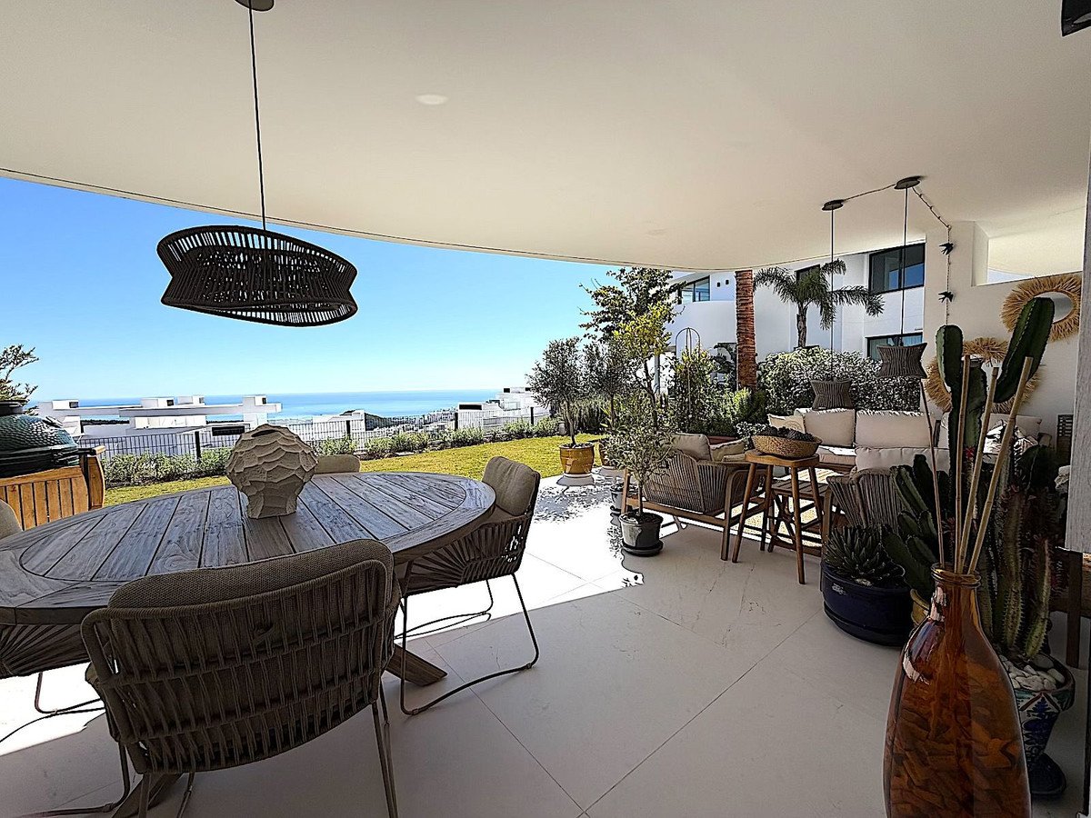 Covered patio with dining table and lounge seating, overlooking ocean and greenery.