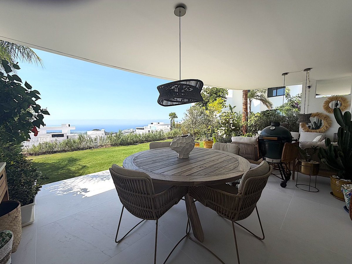 Covered outdoor dining area with round table and chairs overlooking the sea