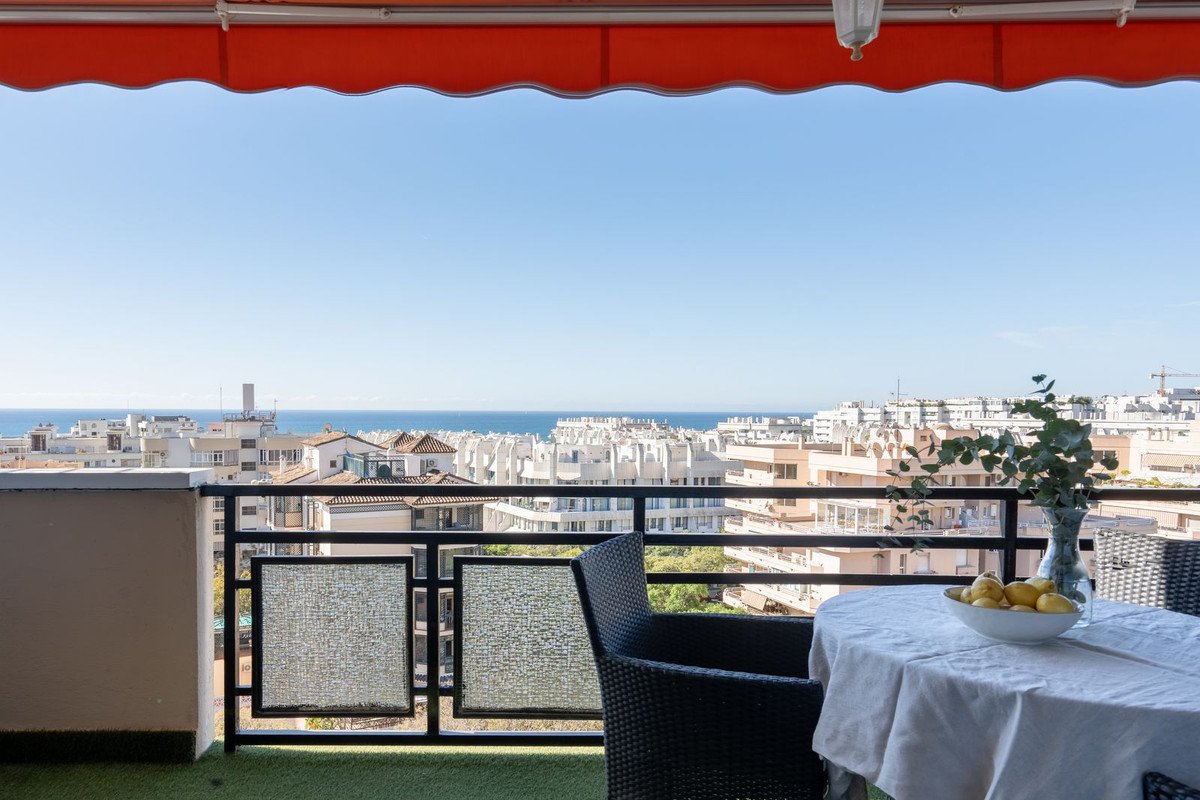 Balcony with sea and city views, featuring a table set for dining outdoors under a red awning.