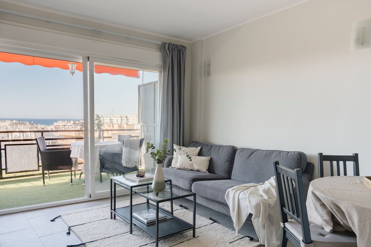 Cozy living room with grey sofa and balcony access overlooking the sea and city skyline.