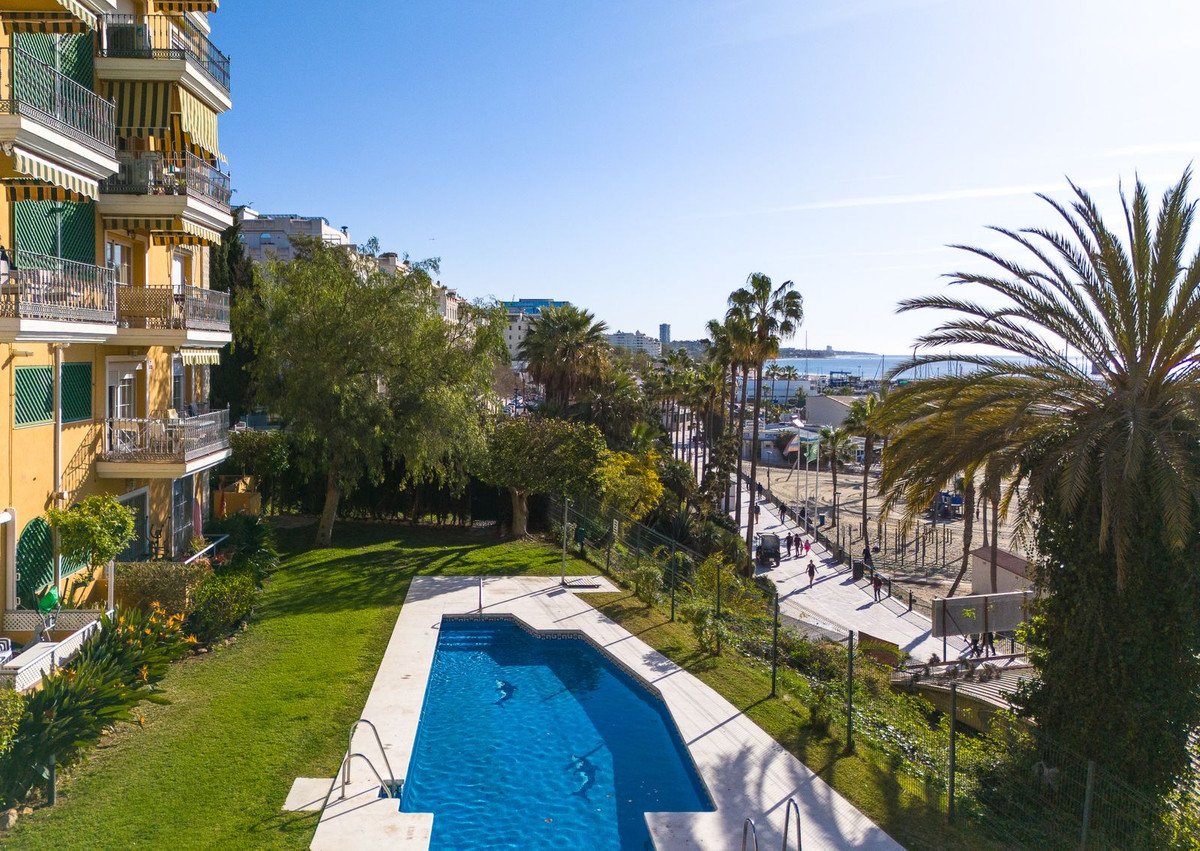 Aerial view of a sunny apartment complex with a pool, palm trees, and a beachfront view.