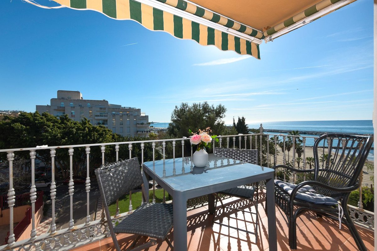 Balcony with table and chairs, ocean view, green and yellow awning, sunny day.