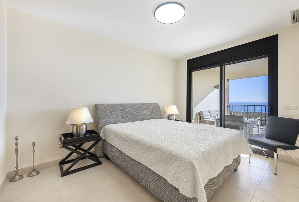Modern bedroom with ocean view through glass doors, gray bed, white bedding, and two lamps.