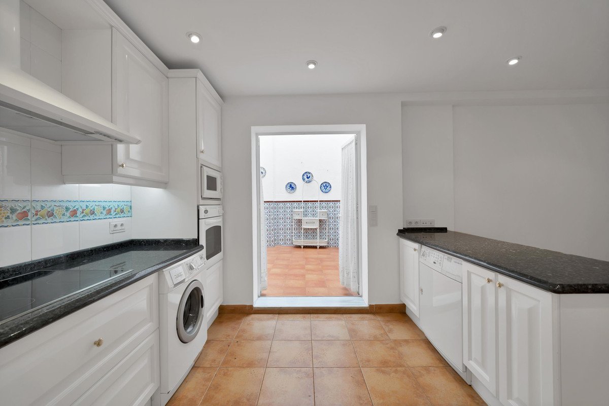 White kitchen with black countertops, tiled floor, and doorway to tiled patio with blue decor.