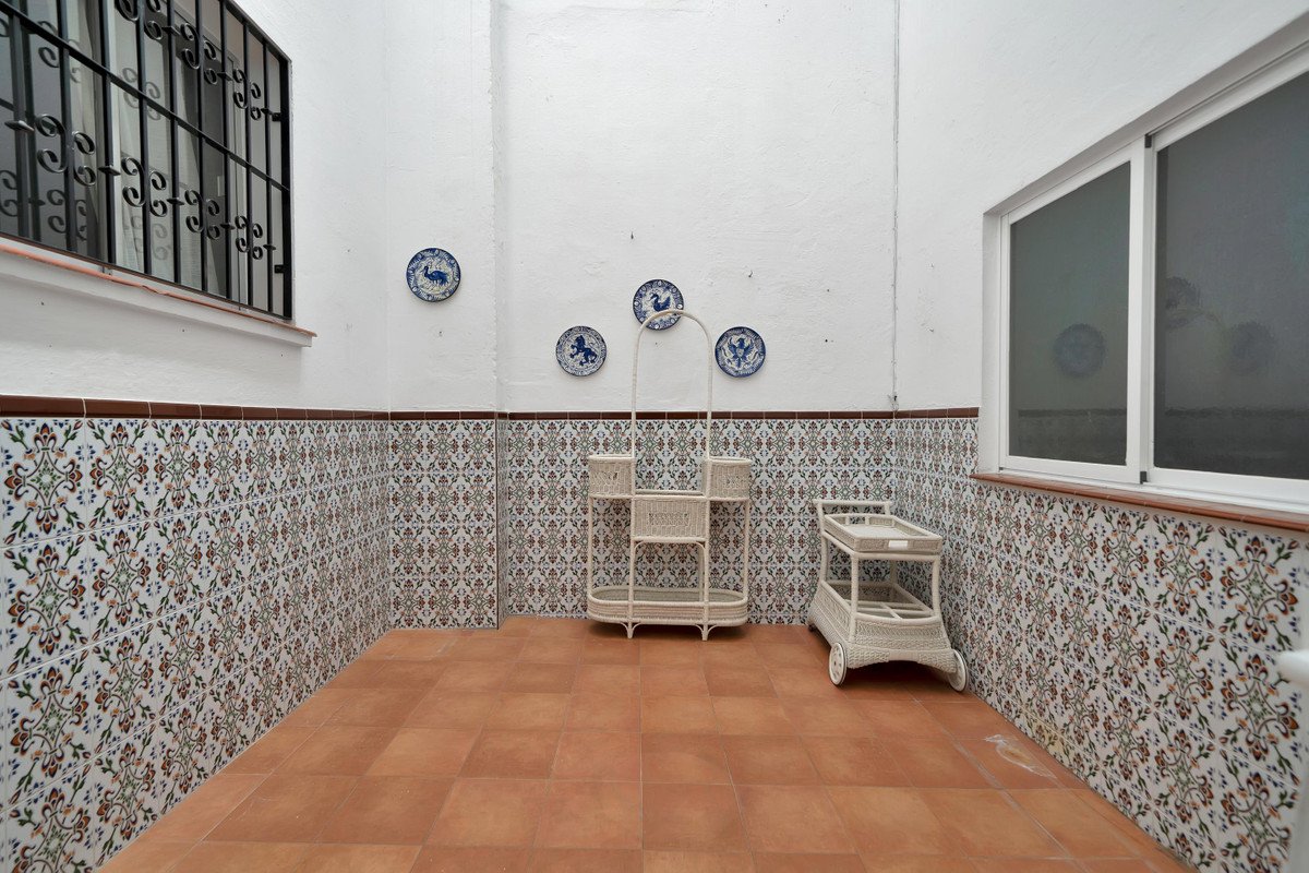 A tiled patio with white walls, decorative plates, and wicker furniture.