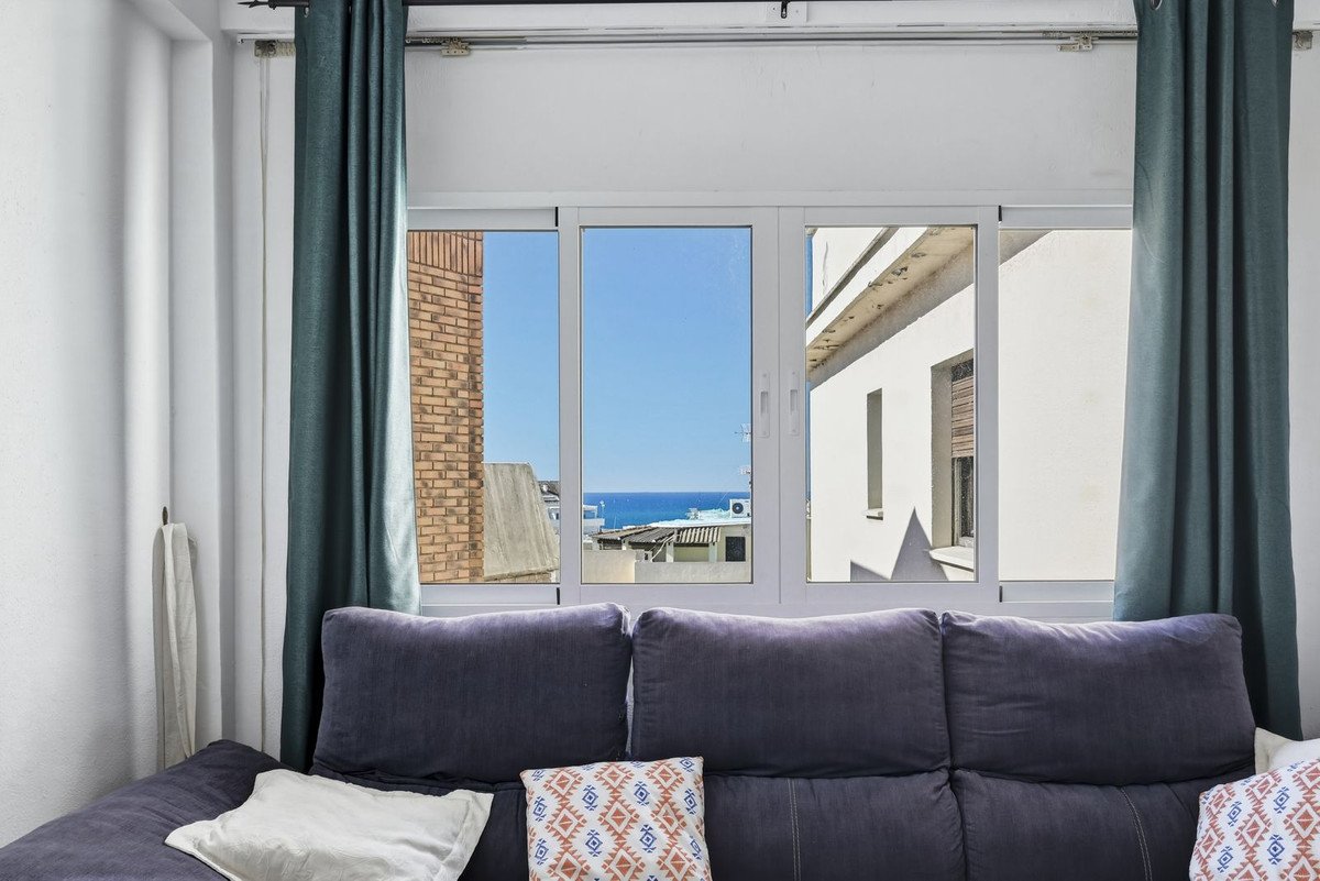 Living room with purple sofa, large window offering ocean view, and dark green curtains.