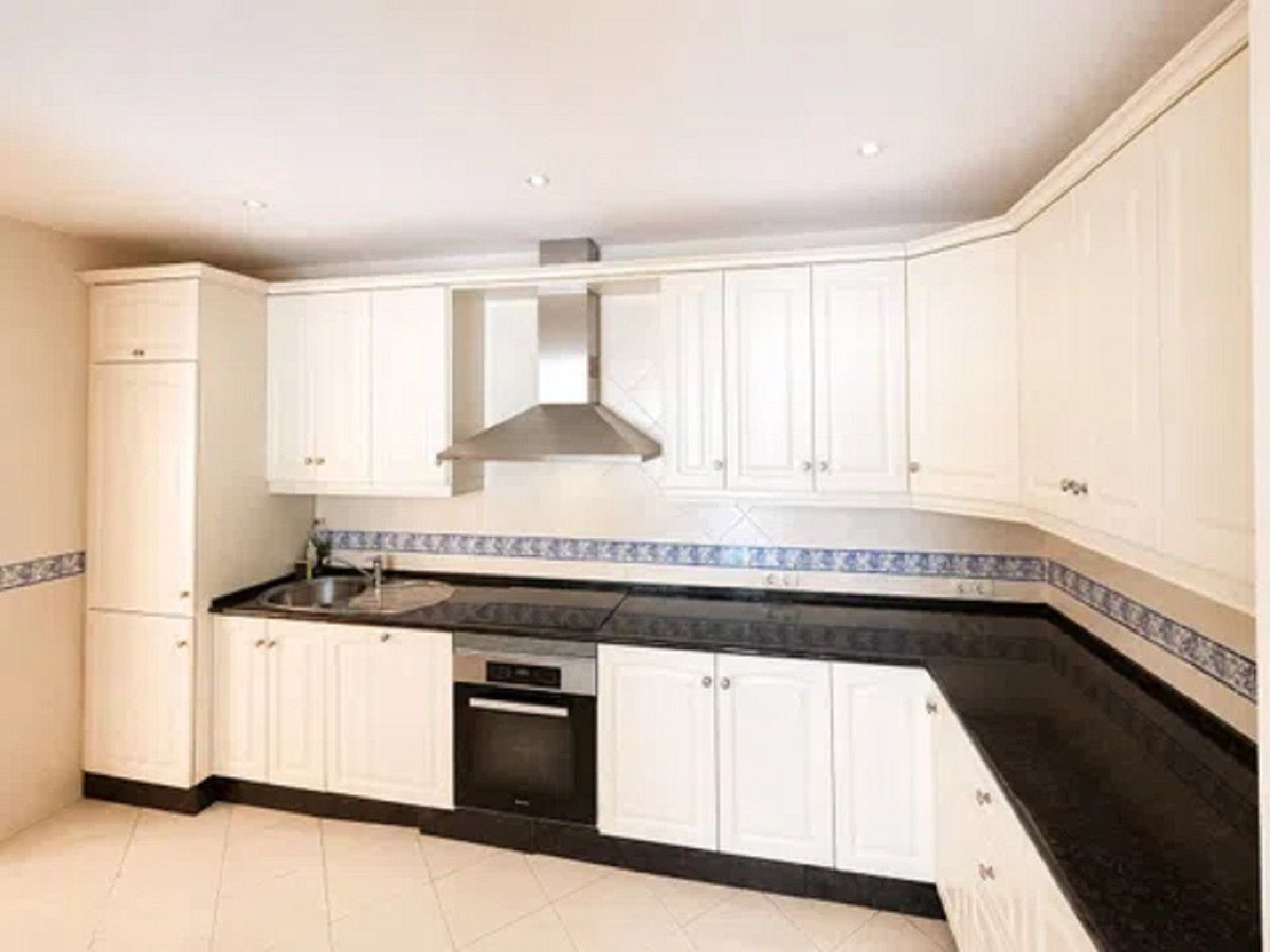A modern kitchen with white cabinets, black countertops, a built-in oven, and a stainless steel range hood.