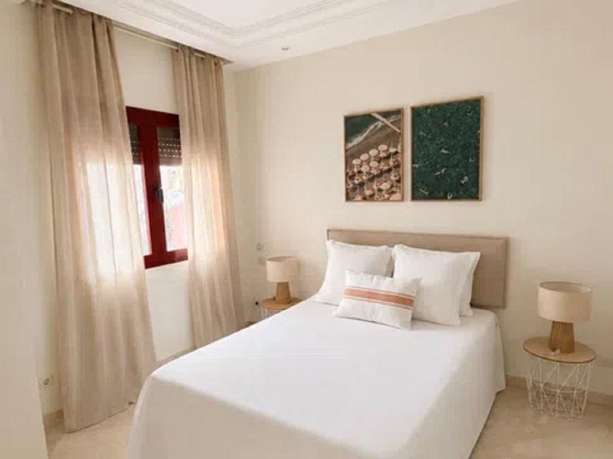A well-lit bedroom with a double bed, white linens, sheer curtains, and modern wall art above the headboard.