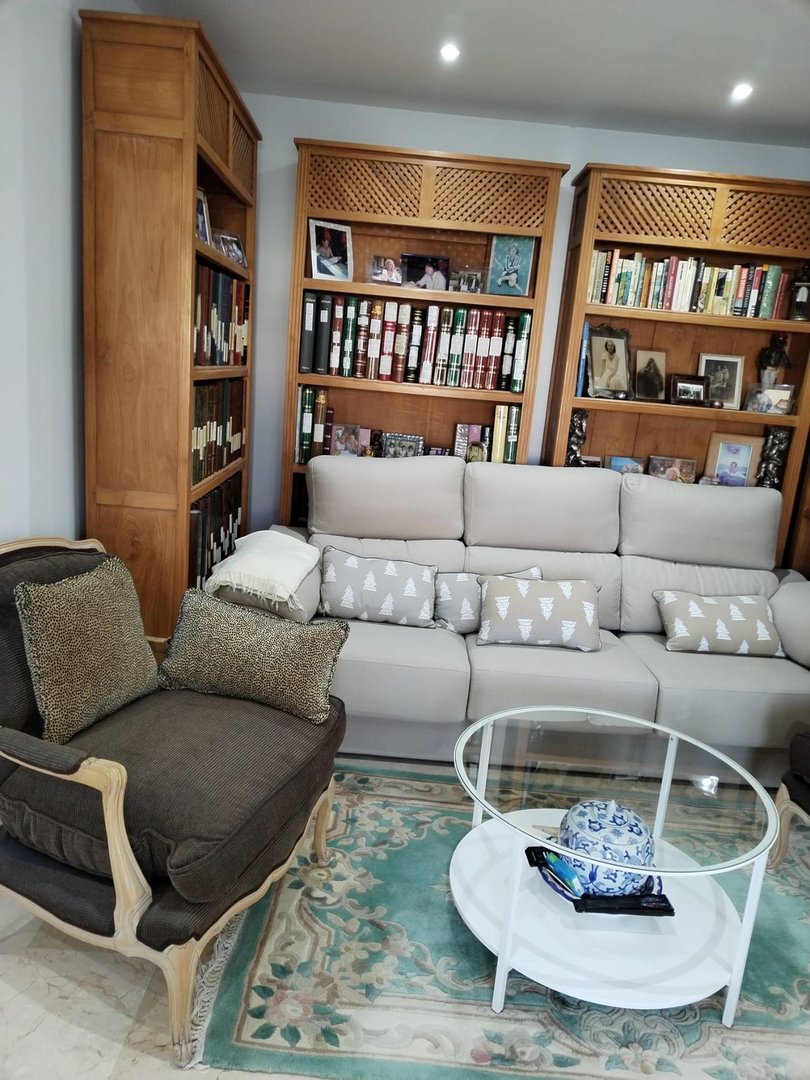 Living room with beige sofa, wooden bookshelves, glass coffee table, and patterned rug.