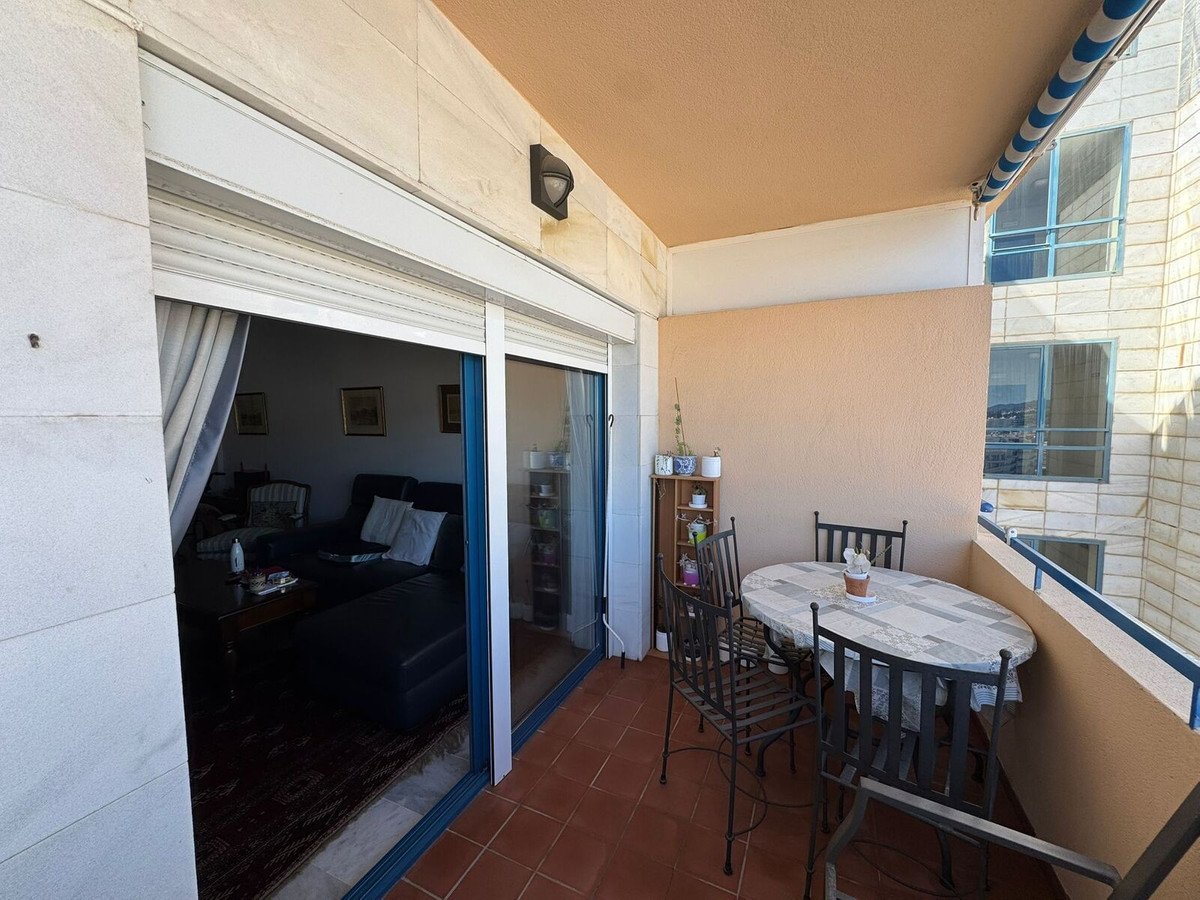 Balcony with table and chairs, glass doors to living room, tiled floor, city view.