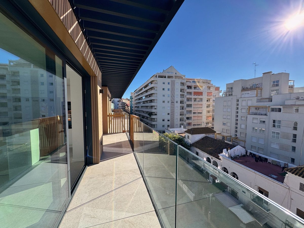 Modern balcony with glass railing and city views, featuring wooden accents and a covered area. Sunny day.
