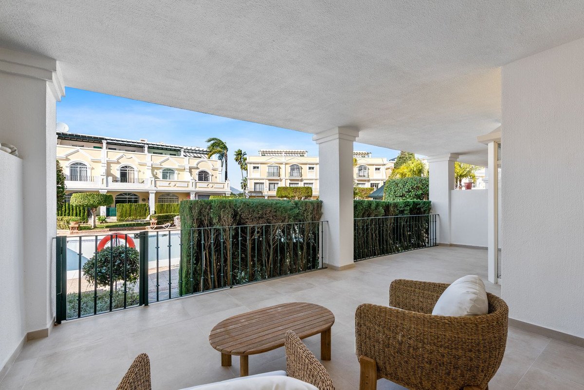 Spacious covered terrace with seating and a view of the pool and surrounding buildings.