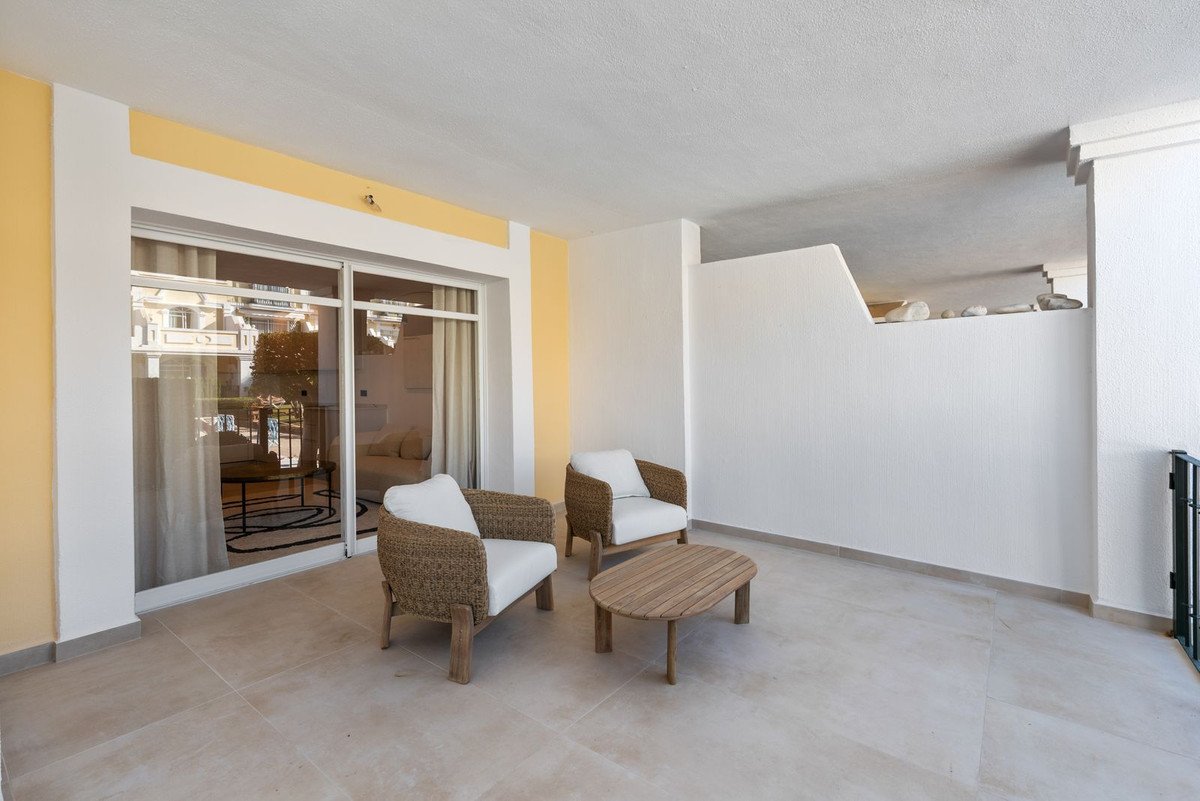 A covered terrace with two woven armchairs and a wooden coffee table, offering a view into a modern living space.