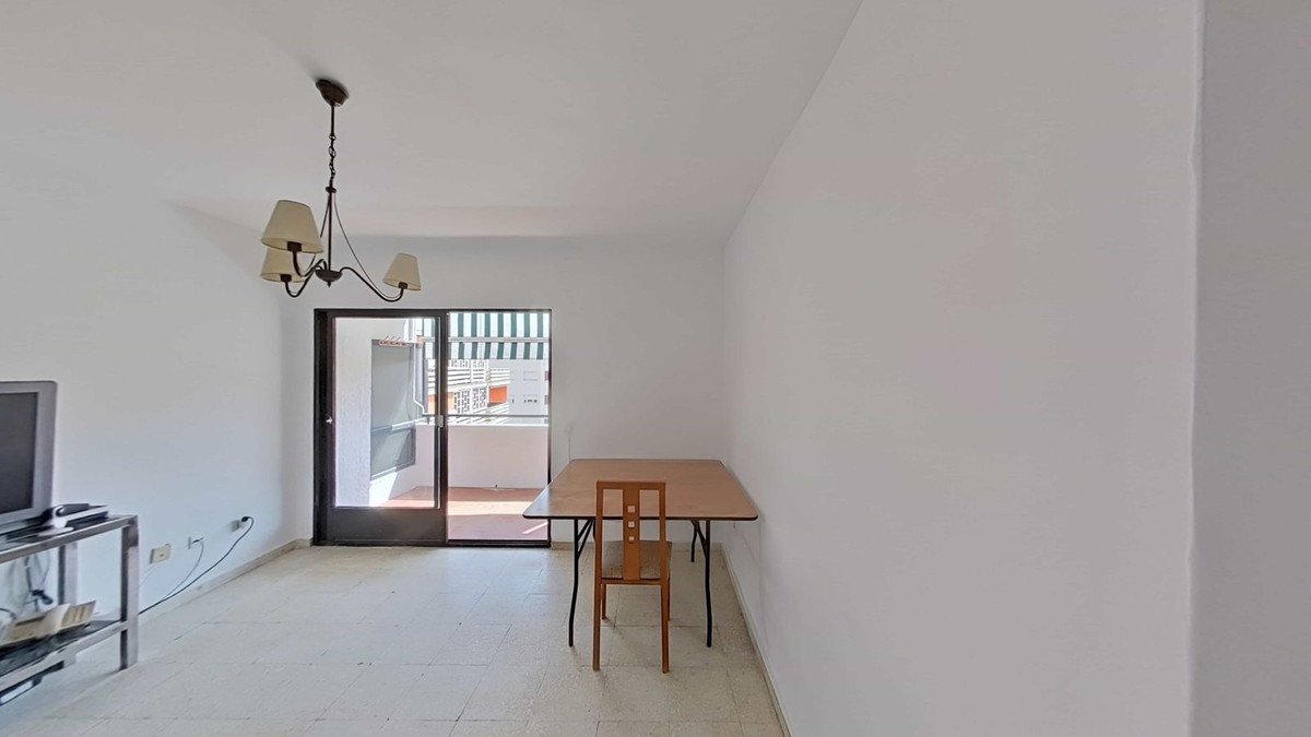 Interior view of a living room with a dining table and chair, leading to a balcony with striped awnings.
