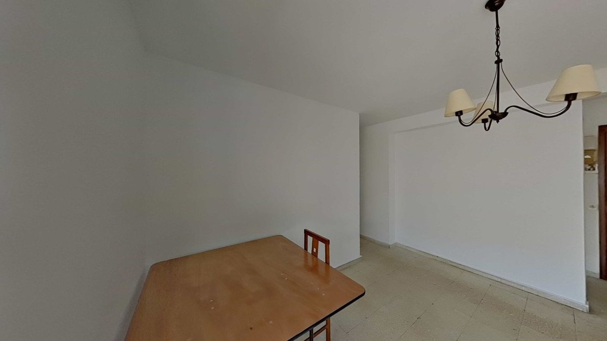 Empty dining room with a wooden table, chair, and chandelier hanging from the ceiling. White walls and tiled floor.